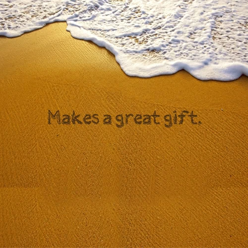 Text "Makes a great gift" written in sand with a wave approaching, offering a moment of beauty perfect for custom framing.