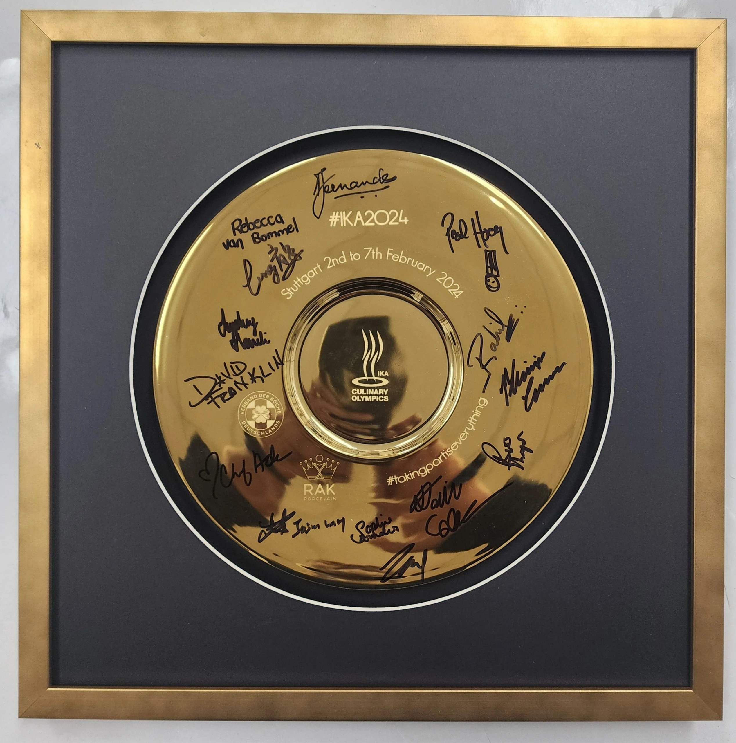 Golden circular plaque with signatures and a Culinary Conversations logo, elegantly set in custom framing of black and gold. Event dated February 2-7, 2024, hashtag #IKA2024 present.