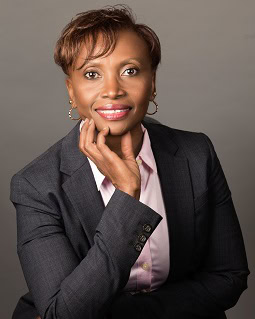 A person in a dark blazer and light shirt smiles while resting their chin on their hand, set against a plain background that subtly suggests the elegance of custom framing.