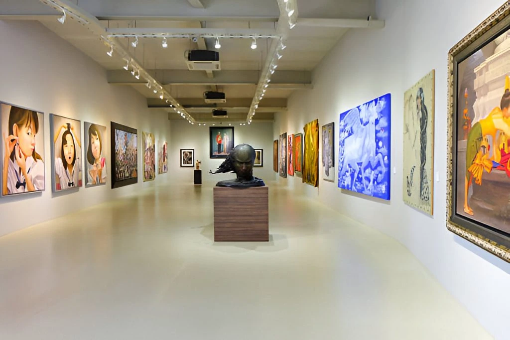 A modern art gallery with a variety of colorful paintings in custom picture frames adorning both side walls and a central sculpture on a pedestal.